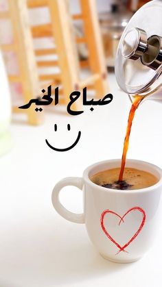 coffee being poured into a white cup with a smiley face drawn on the foam in arabic