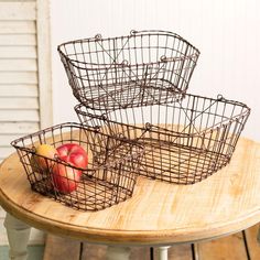 two wire baskets sitting on top of a wooden table next to an apple and another fruit