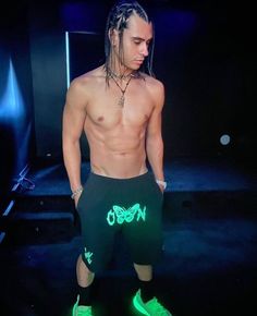 a shirtless man with dreadlocks and neon green shoes standing in the dark