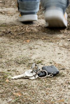 two keys laying on the ground next to a pair of shoes and a person's foot