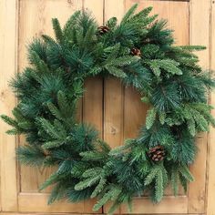 a wreath is hanging on the front door with pine cones and evergreen leaves around it