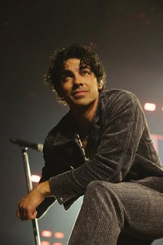 a young man sitting on top of a stool in front of a microphone at a concert