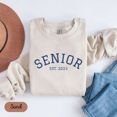 Congratulations Class of 2023! We have cute trendy Senior sweatshirts for class of 2023! Perfect for gifting any graduate!  GILDAN 18000 Unisex heavy blend crewneck sweatshirt Made from polyester and cotton. The collar is ribbed knit, so it retains its shape even after washing.  There are no itchy side seams on these sweatshirts Rolled Sleeves in pictures is for styling purposes only Props used in photos are NOT included with purchase PRINT This is a Direct-to-Garment printed item The ink is printed INTO the fabric, not sitting on top of it Please note that the size of the print/design scales up or down according to the size of the sweatshirt Colors on the screen may vary due to screen color variation and picture lighting SIZE Unisex Adult Size Please refer to our size charts on our thumbn Casual Crew Neck Sweatshirt For Graduation, Casual Letter Print Sweatshirt For Graduation, Casual Long Sleeve Tops For Graduation, Congratulations Class Of 2023, Senior Sweatshirts, Gift For Graduate, Picture Lighting, Sweatshirt Colors, Senior 2023