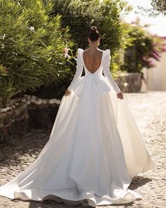 a woman in a white wedding dress is walking down the street with her back to the camera