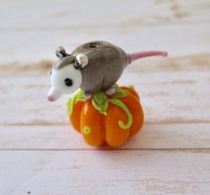 an animal figurine sitting on top of a small pumpkin with a mouse on it