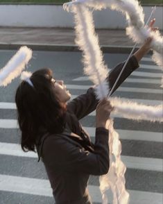 a woman is holding white feathers in the air while she stands on a crosswalk