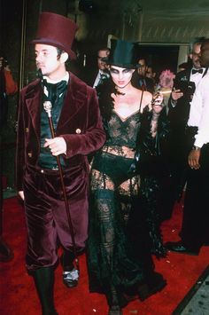 a man and woman dressed in costume walking down a red carpeted area with other people