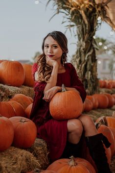 a woman in a red dress is sitting on hay with pumpkins around her and looking at the camera