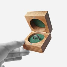 a hand is holding a wooden box with an object inside it that looks like a ring