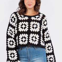 a woman wearing a black and white crochet sweater with flowers on the sleeves