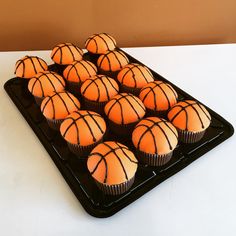 cupcakes with orange frosting in the shape of basketballs on a black tray