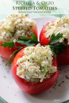 three stuffed tomatoes on a white plate topped with shredded cheese and garnished with fresh herbs