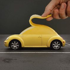 a hand is holding a sponge over a yellow toy car in a parking lot with white lines