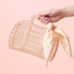 a woman's hand holding a pink purse with a white bow on it, against a pastel background