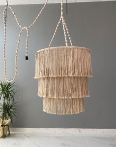 two hanging lights made out of rope and beads on a wall next to a potted plant