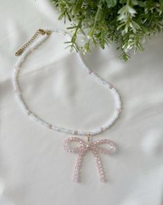 Measurements: 16 to 18.5 inches long Total Weight: 0.45 oz Add a sweet and playful touch to your look with this charming bow necklace, crafted from pink and white glass beads. The delicate bow design brings a whimsical flair, while the shimmering beads catch the light beautifully. Finished with a durable stainless steel clasp, this necklace combines elegance and practicality, making it perfect for everyday wear or adding a dash of fun to special occasions. It's a unique, handcrafted piece that's both eye-catching and timeless. Cute White Necklace With Round Beads, Party Jewelry With Pink Bow In White, Cute White Necklaces With Round Beads, White Jewelry With Pink Bow For Party, White Party Jewelry With Pink Bow, Cute White Jewelry With Beaded Chain, Dainty Pink Beaded Necklaces For Gifts, White Jewelry With Bow For Gifts, Pink Bow Necklace For Party