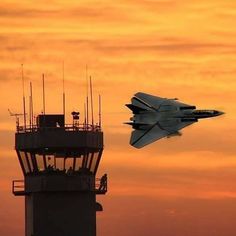 a jet is flying in the sky next to a tower with antennas and lights on it