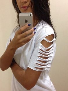 a woman holding a cell phone in her right hand and looking at the camera while wearing ripped white clothing