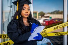 a woman in graduation cap and gown holding a piece of paper next to police tape