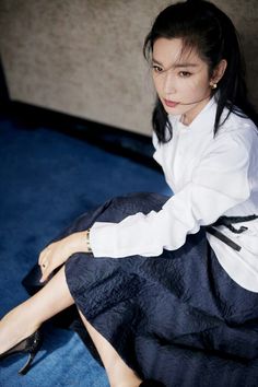 a woman sitting on top of a bed in a white shirt and black skirt with her legs crossed