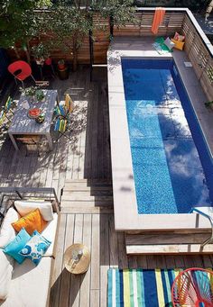 an above ground pool surrounded by wooden decking and patio furniture with colorful throw pillows