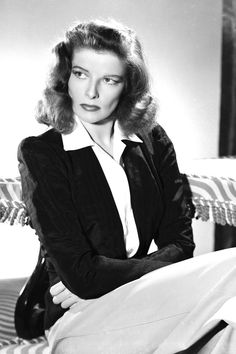 a woman sitting on top of a bed in a black jacket and white dress shirt