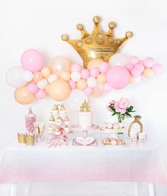 a table topped with lots of pink and white balloons next to a gold crown on top of a wall