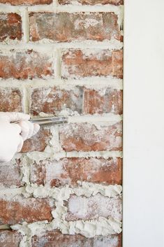 a person in white gloves is using scissors to paint a brick wall with white paint