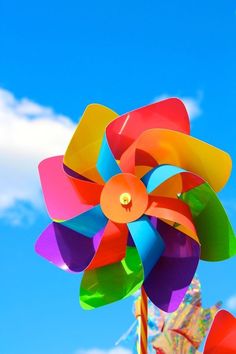 a colorful pinwheel is in the foreground against a blue sky with white clouds