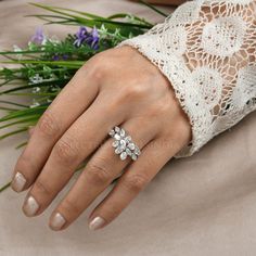 a close up of a person's hand with a ring on it and flowers in the background