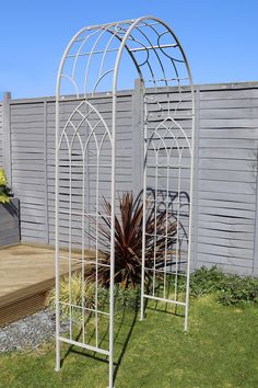 a white metal garden trellis sitting on top of a grass covered yard next to a wooden deck