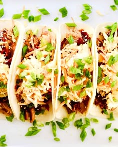 four tacos are lined up on a white plate with green garnishes