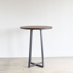 a round wooden table sitting on top of a cement floor next to a white wall