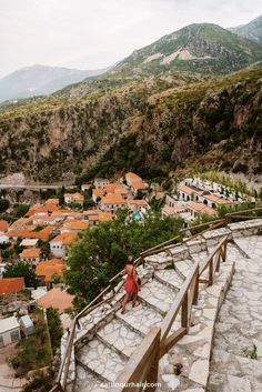 a woman walking up some stairs in front of a village and mountains with houses on the other side