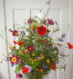 a vase filled with lots of colorful flowers sitting on top of a wooden table next to a white door