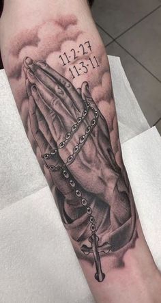 a person with a rosary and praying hands tattoo on their arm is holding the cross