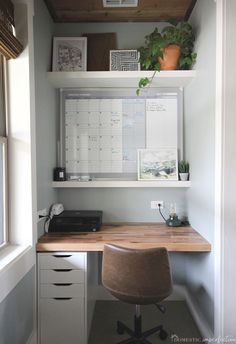 an office with a desk, chair and calendar on the wall above it is also a potted plant