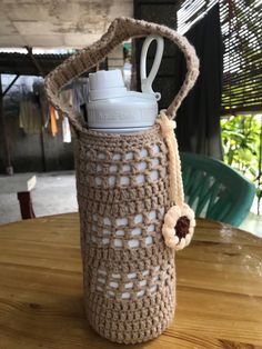 a crocheted water bottle holder sitting on top of a wooden table