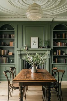 a dining room with green painted walls and wooden table surrounded by chairs, bookshelves and shelves