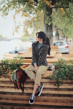 a young woman sitting on top of a wooden bench next to a tree and water