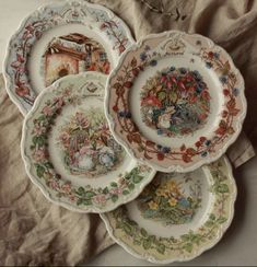 four plates with different designs on them sitting next to each other in front of a piece of cloth