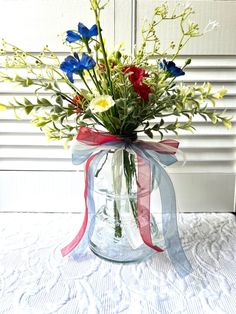 a vase filled with flowers sitting on top of a white table covered in lace and ribbon