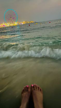 a person's feet in the water with a ferris wheel in the back ground