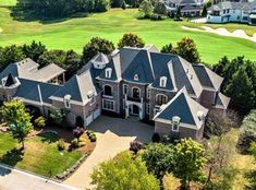 an aerial view of a large house with lots of trees in the foreground and golf course behind it