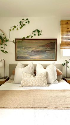 a bed with white linens and pillows in front of a painting on the wall