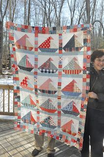 a woman standing on a deck holding up a quilt