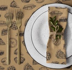 a place setting with napkins, fork and knife on a tablecloth covered plate