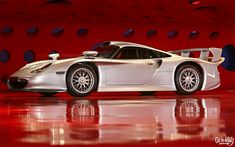 a silver sports car parked in front of a red wall