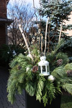 a white lantern and pine cones in a black planter on the side of a house