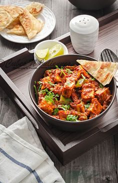 a pan filled with food sitting on top of a wooden table next to plates and utensils